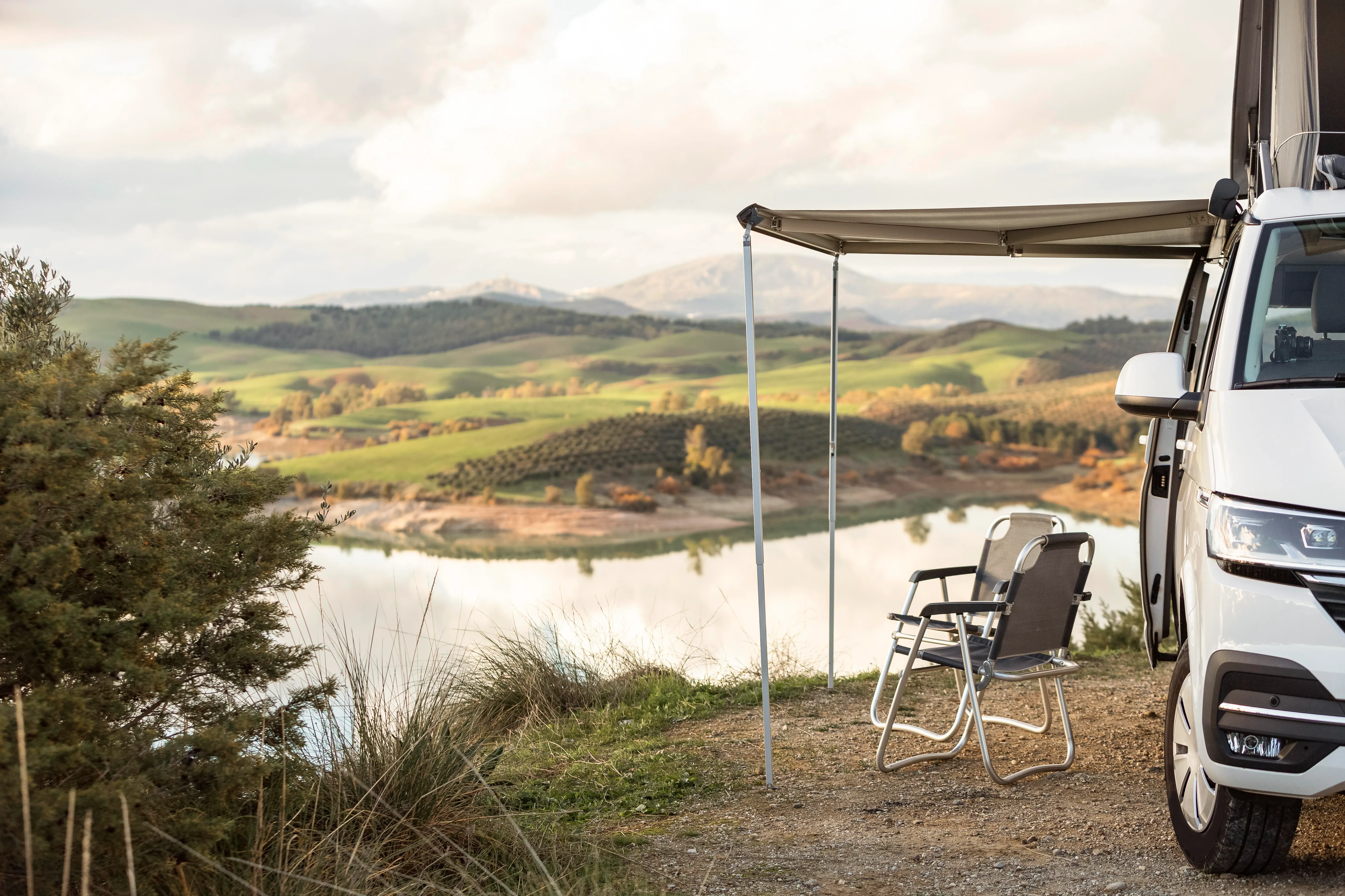 Campervan with two camping chairs overlooking a lake and rolling countryside