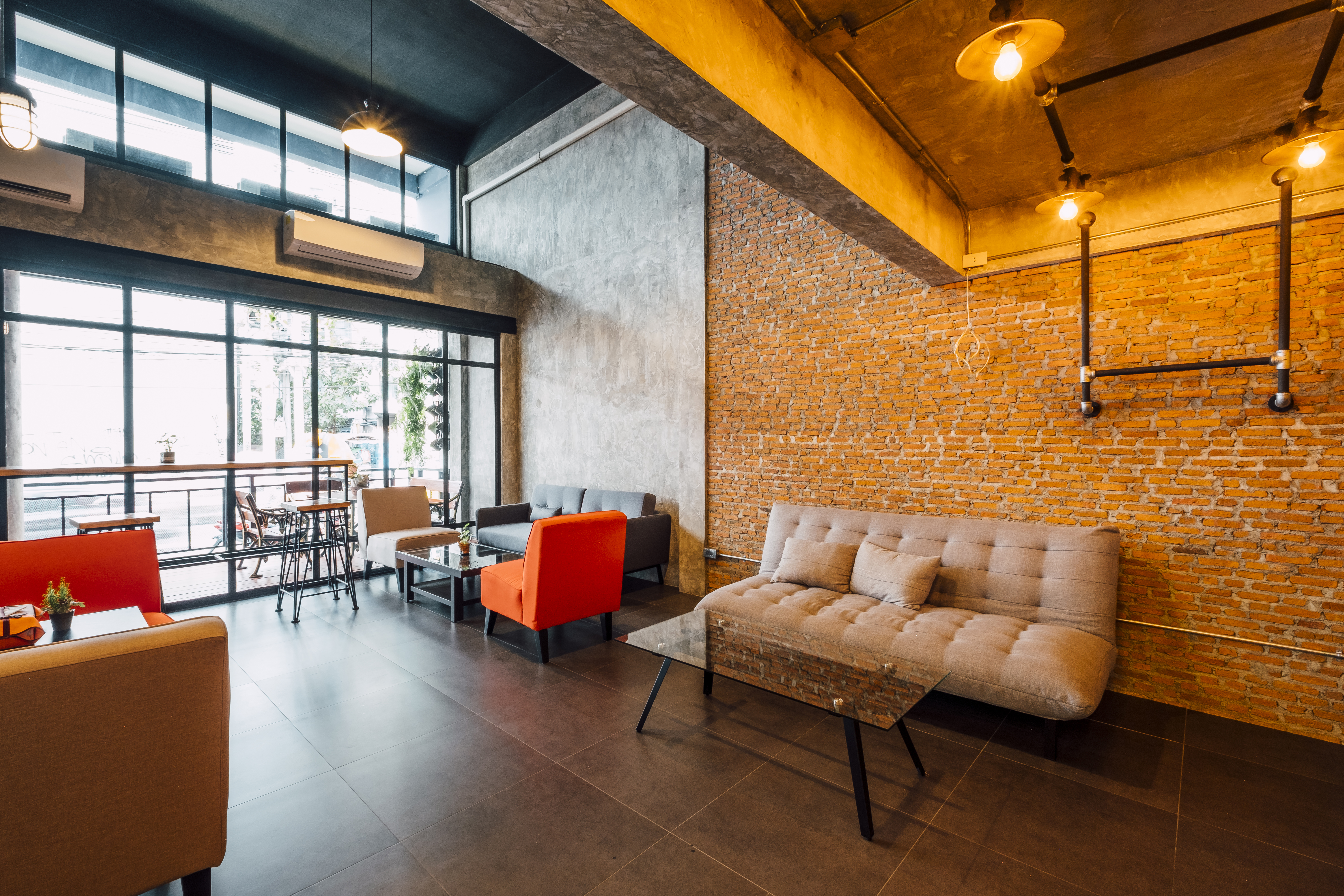 Flexible modern workspace with sofas, armchairs and tables beneath warm lighting and exposed brick walls