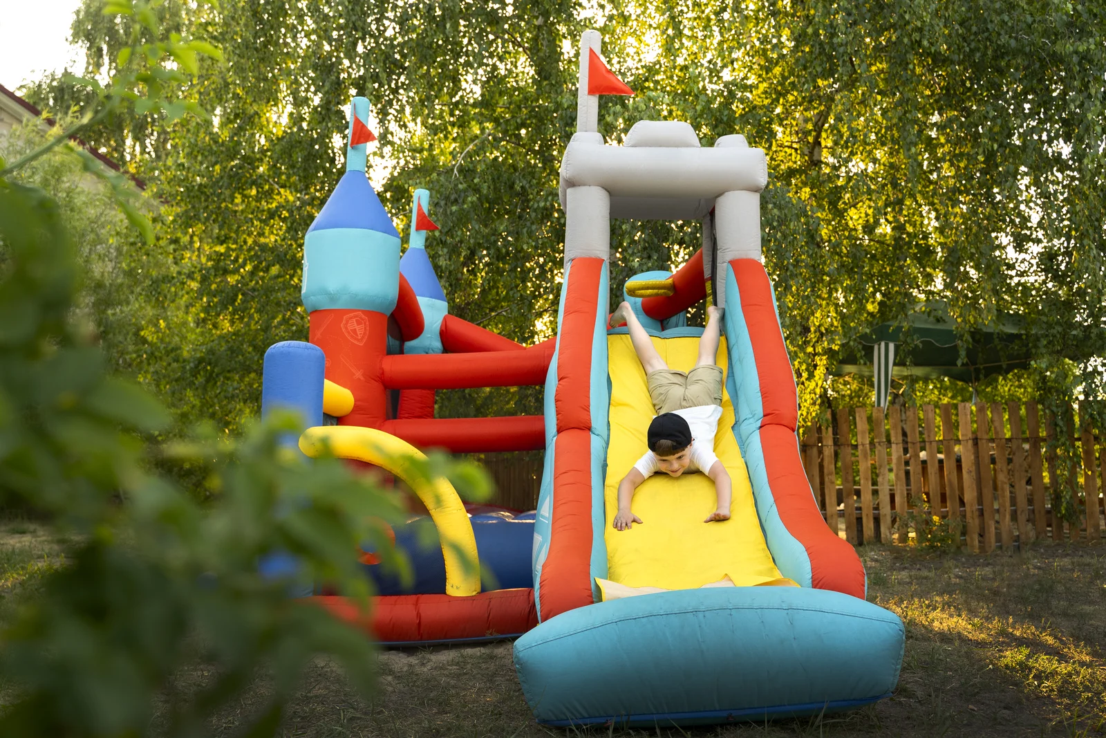 Child playing on a colourful inflatable bouncy castle slide in a leafy garden